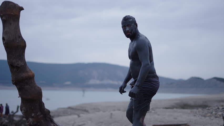 Boy covered in mud all over looks at the camera in a reservoir