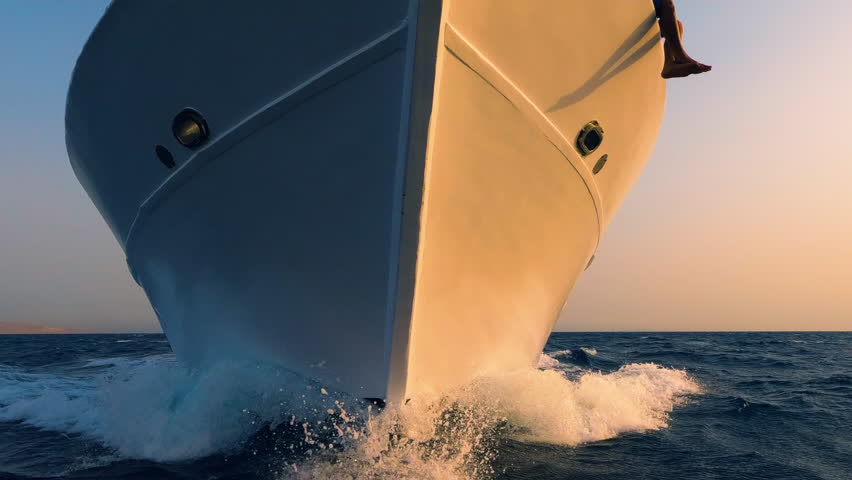 Sailboat prow breaking sea water front view, white foam and splashes close up. Yachting, ocean sailing, sunset sun light on vessel part, boat forepart closeup