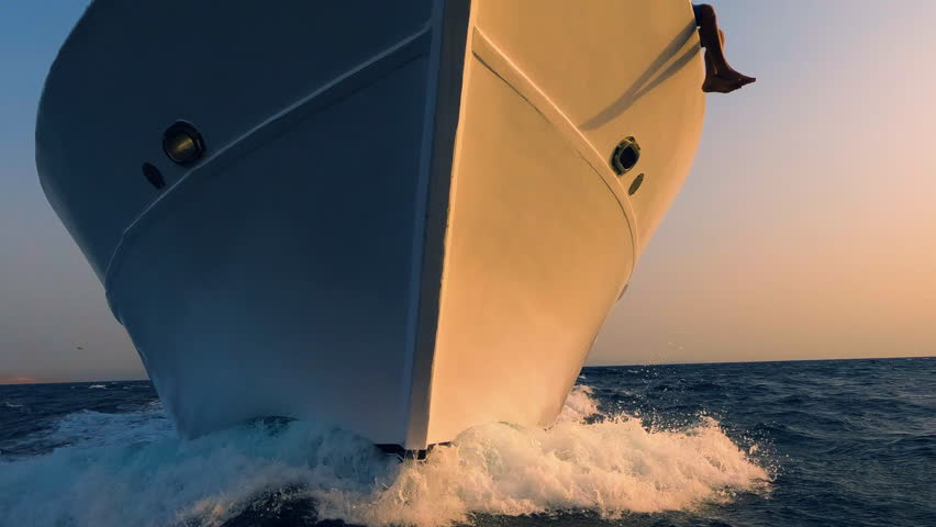 Sailboat prow breaking sea water front view, white foam and splashes close up. Yachting, ocean sailing, sunset sun light on vessel part, boat forepart closeup