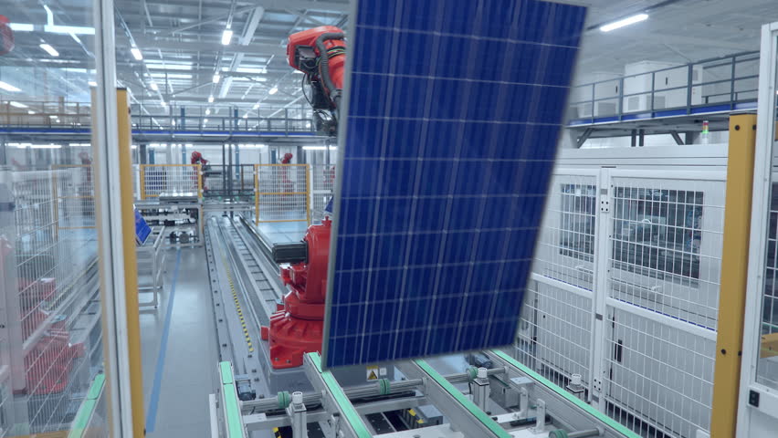 Orange Industrial Robot Arm Moving Solar Panels at Production Line at Modern Bright Factory. Solar Panels are being Assembled on Conveyor. Automated Manufacturing Facility. POV view from the Line