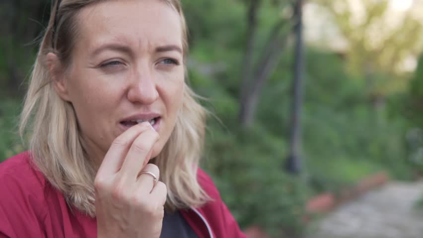Close-up, a woman chews gum outside.