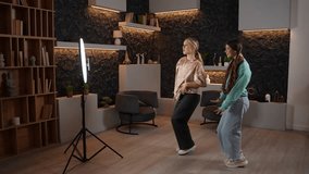 Side view of pretty teen girls dancing and recording video for social media. Two young beautiful women dancing hip hop popular dance for online channel and having fun at home. High quality footage