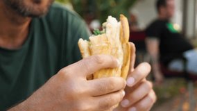 A blurred video of a bearded man biting the mouth of a sandwich in close-up. A man eating in an outdoor café. The concept of eating outdoors