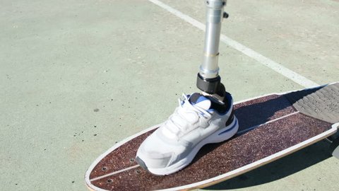 Closeup shot of man with prosthetic leg skateboarding outdoors. Skillful man with disability using artificial leg for doing sports on warm summer day at sportsground. Amputee sport, disability concept Video Stok