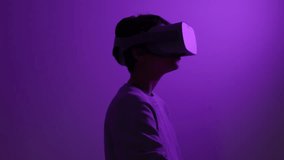 Teenager wearing futuristic virtual reality headset reaching out in purple lit room