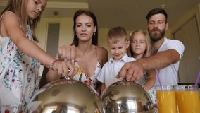 Happy parents with children, son and twin girls, have breakfast in a hotel room sitting on a small sofa, dad lifts the metal lid to reveal the dish. - Powered by Shutterstock - Get 15% off with code: PIKWIZARD15