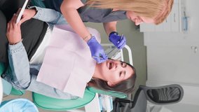 Vertical video Professional Woman Dentist Examines Female Patient with a Special Tool and Prescribes Treatment in a Modern Dental Clinic. Oral Hygiene. Concept of Healthcare and Medicine. Slow Motion