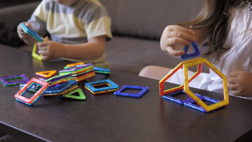 A boy in a gray T-shirt sits on a bed near a white wall and plays with a Ferris wheel, which he designed with a magnetic constructor. Creativity development. Magnetic constructor. Carefree weekend.