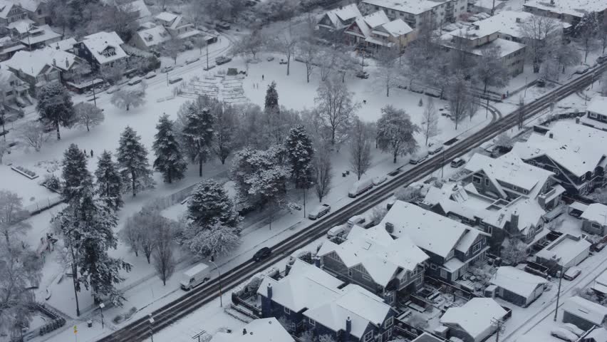 Fly over Vancouver disctrict with house roofs in snow and cars on a snowy road