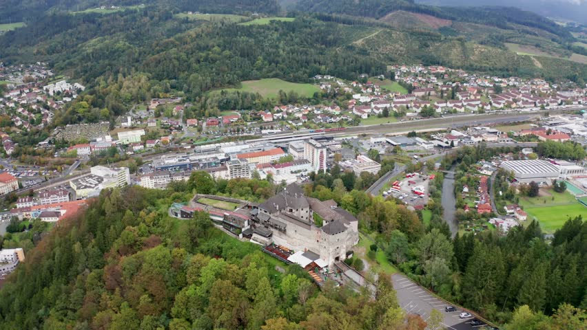 aerial photography, wide drone establishing shot of Burg Oberkapfenberg castle in Kapfenberg Austria, with the city in the background, circling around the castle from a wider distance