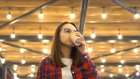 A young woman walks with coffee in a cafe against the background of a ceiling made of paws. A girl with glasses walks along a cozy alley in a cafe. Slow motion.