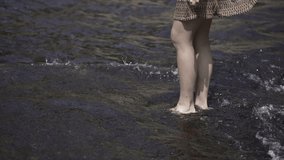 Young european girl kicks the water twice in the seaside barefoot.