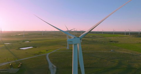 4K aerial wind turbine shot flying over top and through the blades revealing a green pasture and a blue and pink sunset in this sustainability concept on a wind farm. Arkistovideo