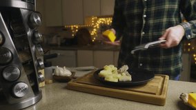 Video. A man rubs cheese on a manual grater on cooked potatoes with meat. Garlic and kitchen appliances are on the table. Home kitchen interior. Delicious and appetizing meals.
