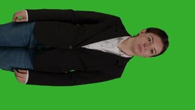 Vertical video: Front view of professional manager pointing aside to show advertisement over greenscreen studio backdrop, creating example ad on blank copyspace. Young adult with suit showing ad icon