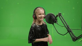 close-up of portrait of young girl singing into a studio microphone on a green screen background.