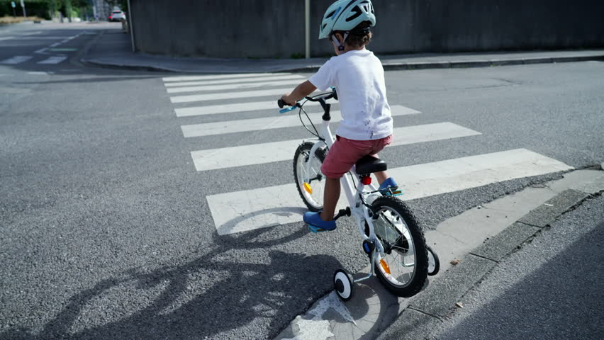 Young cyclist crossing street on crosswalk zebra lines. Child rides bicycle outdoors with wheels and helmet. Sportive kid exercising in city