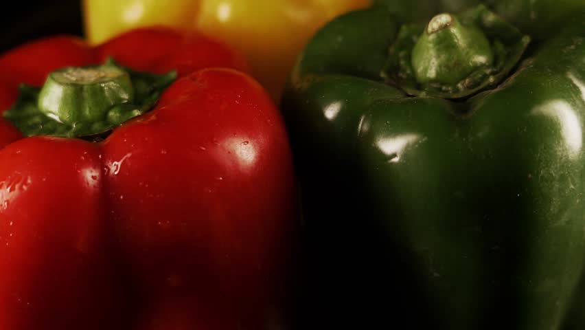 Paprika peppers on a black background with water drops. Red green and yellow sweet bell pepper is rotating shot 4k Royalty-Free Stock Footage #1098111303