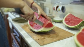 Female hands that cut watermelon on a wooden board with a knife in the kitchen