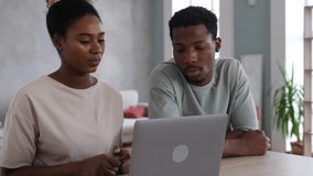 A happy young family is sitting in a cozy living room with a laptop, a positive man helps his woman figure out the problem. - Powered by Shutterstock - Get 15% off with code: PIKWIZARD15