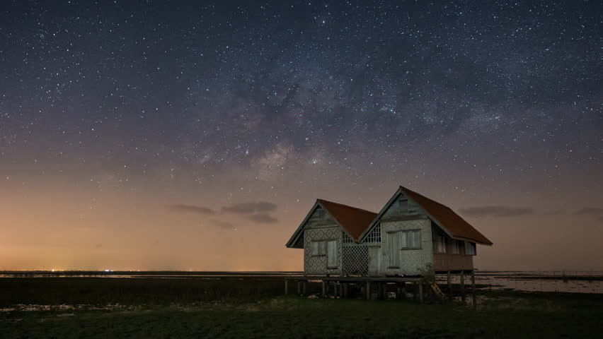 Zoom out time lapse of milky way and stars above the abandoned twin house near the lake with clear night sky