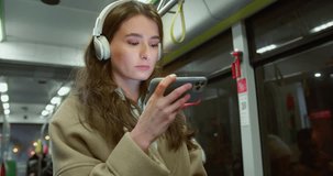 Portrait stylish serious young woman riding bus watching videos online on smartphone and headphones. Beautiful calm cute female adult girl enjoying ride standing in public transport. Wireless concept.