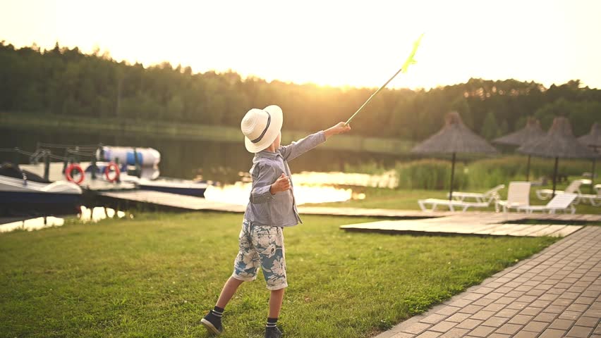 A boy in a hat at sunset plays with scoop-net outdoors on a summer day. Summer outdoor activities for children. Royalty-Free Stock Footage #1098127419