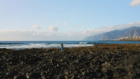 Girl traveler explores rocky beach with wide foaming waves and huge cliffs on the background. Woman enjoys ocean coastline. Tourism, travel, vacation on blue sea. Leisure. - Powered by Shutterstock - Get 15% off with code: PIKWIZARD15