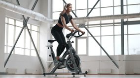 Young, caucasian woman, wearing black sportswear, and sweating in gym. Active, beautiful girl working hard on a stationary bike indoors. High quality 4k footage - Powered by Shutterstock - Get 15% off with code: PIKWIZARD15