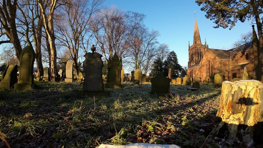 FPV flying around headstones in snowy autumn sunrise cemetery during golden hour