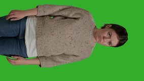 Vertical video: Front view of depressed frustrated person acting sad and displeased, posing over green screen background, being disappointed and discouraged. Upset female model standing over full body