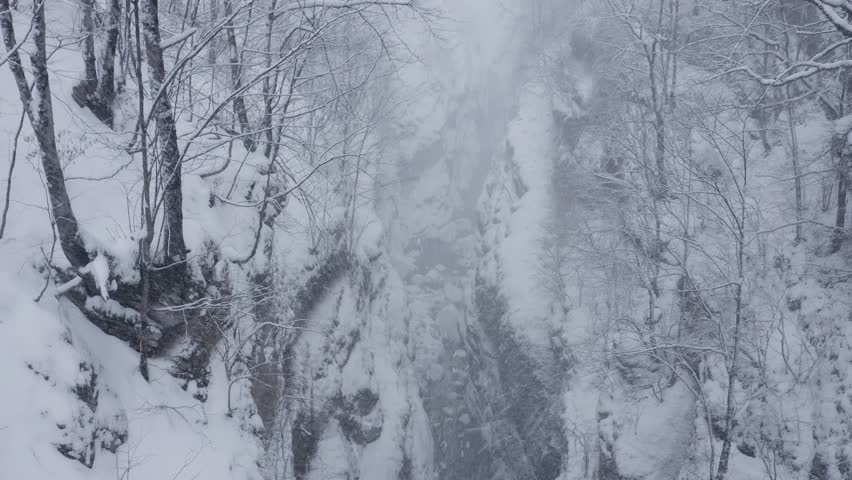 Going up aerial footage of Urukh river canyon and the road running alongside at winter strong snowfall. Digoria, North Ossetia, Russia.