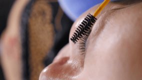 Eyelashes extensions procedure. Vertical video. Hand of master for extension and volumetric extension of long lush eyelashes combs eyelashes with brush. Woman with long lush eyelashes undergoes beauty