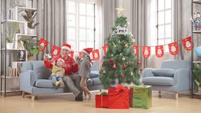Asian Male And His Children Waving Hand Having A Video Call On Smartphone While Celebrating Christmas Together At Home 
