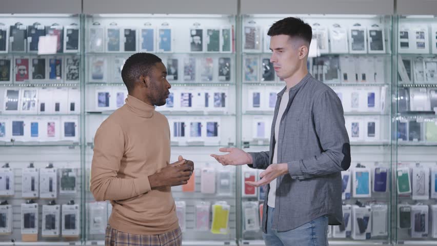 African man in an electronics and gadgets store. The seller-consultant tells the buyer about goods and services. Royalty-Free Stock Footage #1098159639