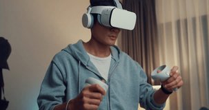 Close-up Young Asian man gamer wear gray hoodie with VR oculus hold VR joystick controllers feeling exciting and fun with new experience of game in living room home at night. Virtual reality concept.