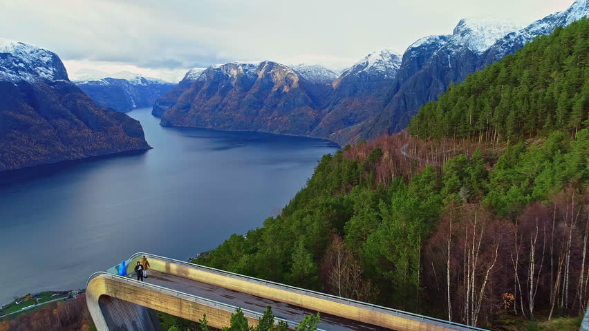 Aerial fly over bridge revealing lush mountains and snow top mountains over the lake in Norway alesund