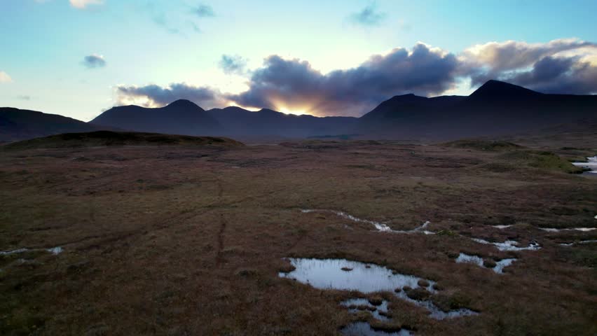 Aerial drone footage flying low and close to the surface of a peat bogs before rising to reveal freshwater lochs and dark mountains on the horizon at sunset. Loch Ba, near Glencoe, Scotland