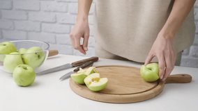 Woman in home clothes cutting apples on cutting board in the kitchen. Preparing healthy food. Hands holding knife and slicing fruits on table in kitchen