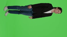Vertical video: Side view of businesswoman doing no sign with palm on camera, expressing disapproval and denial. Young adult in suit showing rejection and refusal gesture over full body greenscreen
