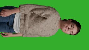 Vertical video: Side view of close up cheerful girl wearing sweater acting lovely over isolated greenscreen backdrop in studio. Modern person being positive and happy, confident model on camera over