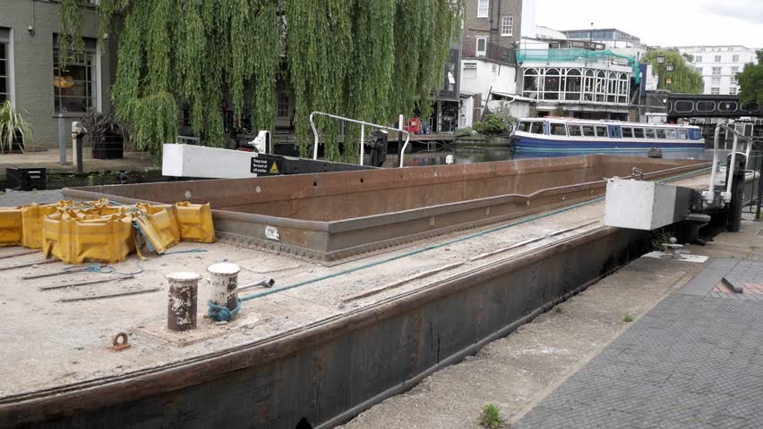 Narrowboat with container for construction and industry transportation being pulled out of lock chamber at Regent's canal. Canal bridge for Camden High street in front. Red bus double-decker. Royalty-Free Stock Footage #1098187533