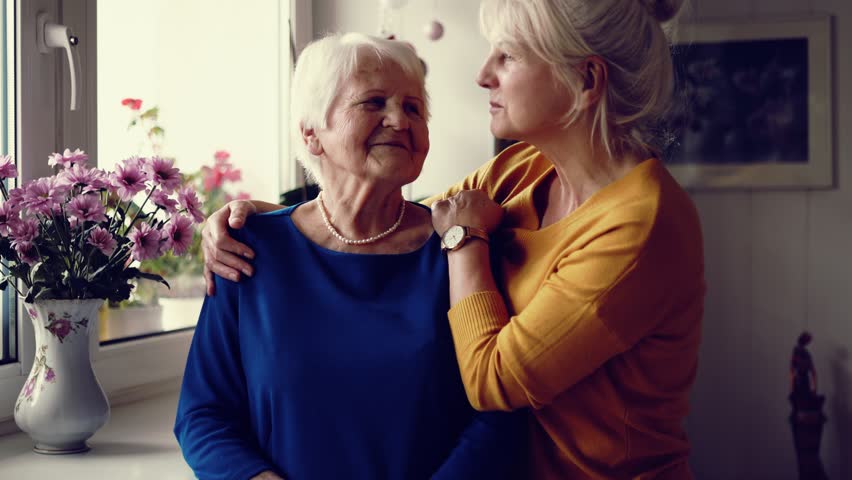 Senior woman holding hands and being consoled by younger woman
