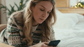 Caucasian woman using phone while lying down on front in bed on Christmas time. Shot with RED helium camera in 8K.  