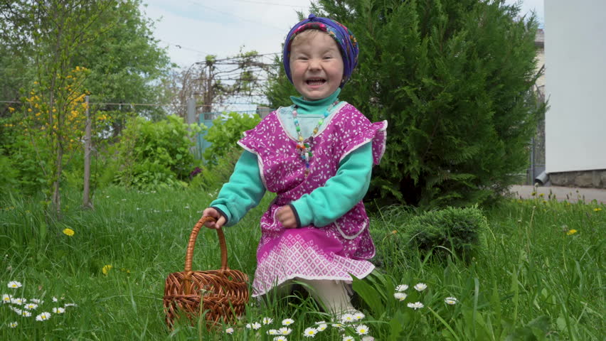 little girl in an apron in spring,a little girl with a basket is playing in the yard on the grass
