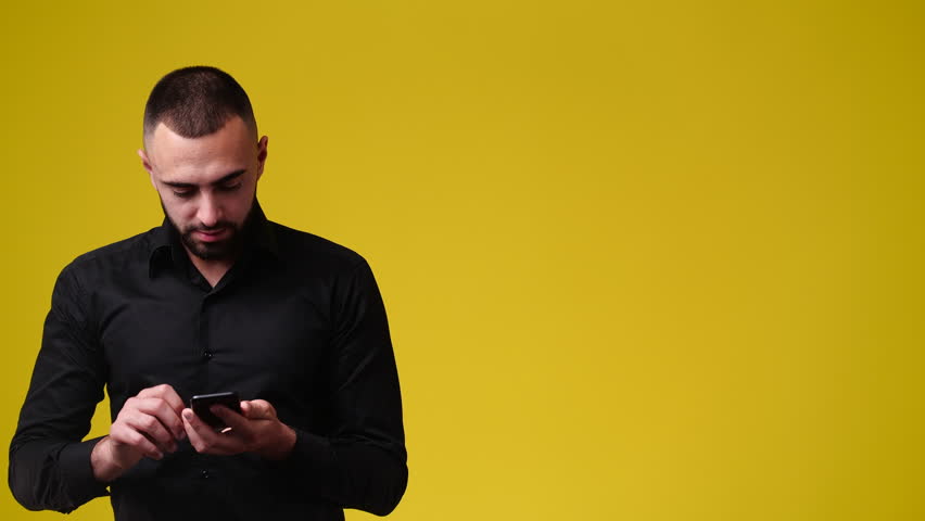 4k slow motion video of man using phone and pointing at right side over yellow background. | Shutterstock HD Video #1098210531