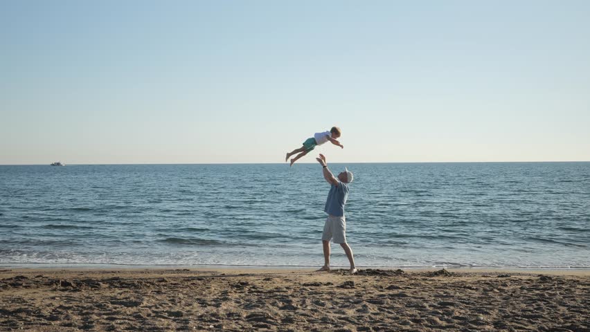 Dad swinging his toddler son into the air on the beach having fun at sunset, father playing with his young son at the beach, priceless parenthood moments, father son silhouette. 4k footage Royalty-Free Stock Footage #1098211337
