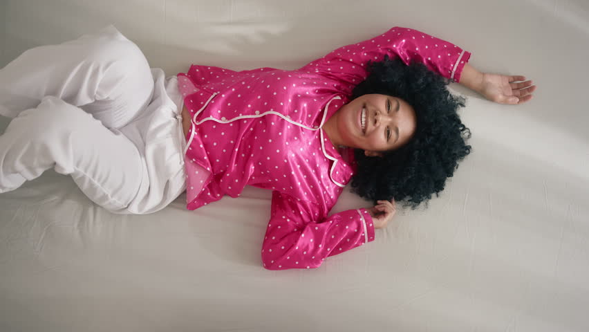 Happy African American woman jumping on bed or sofa laughing enjoying relax. Rest on cozy couch feel overjoyed celebrate weekend or holiday. Woman of color in pajama enjoying vacation morning 4K Royalty-Free Stock Footage #1098212737