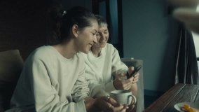Two young women watching funny videos on their smartphone while relaxing together at home