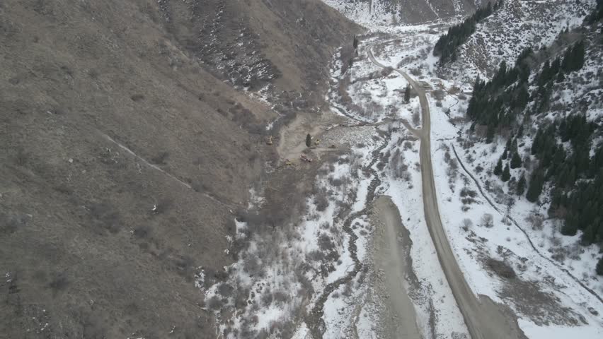 Heavy construction equipment in a mountain gorge is working on the initial stage of building a dam on a river.